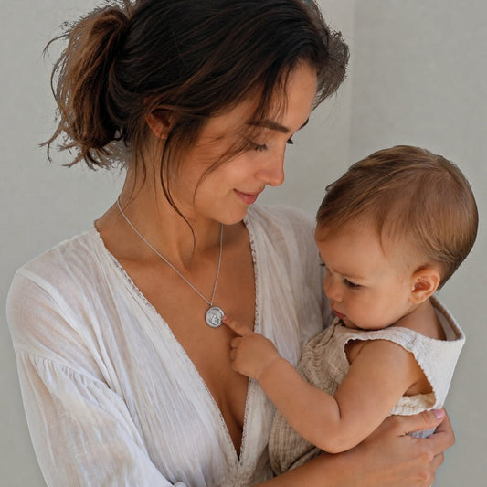 Mujer con bebé usando collar medallón perfumado Moment de acero inoxidable con diseño amor de mamá