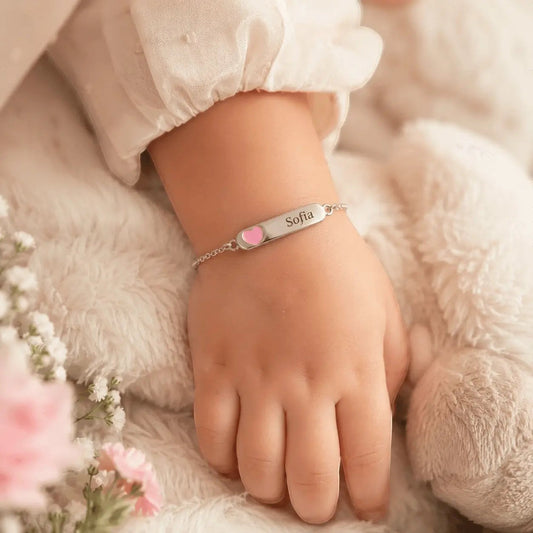 Pulsera Moment de plata para niña con placa grabada y detalle de corazón rosa en la muñeca de un bebé