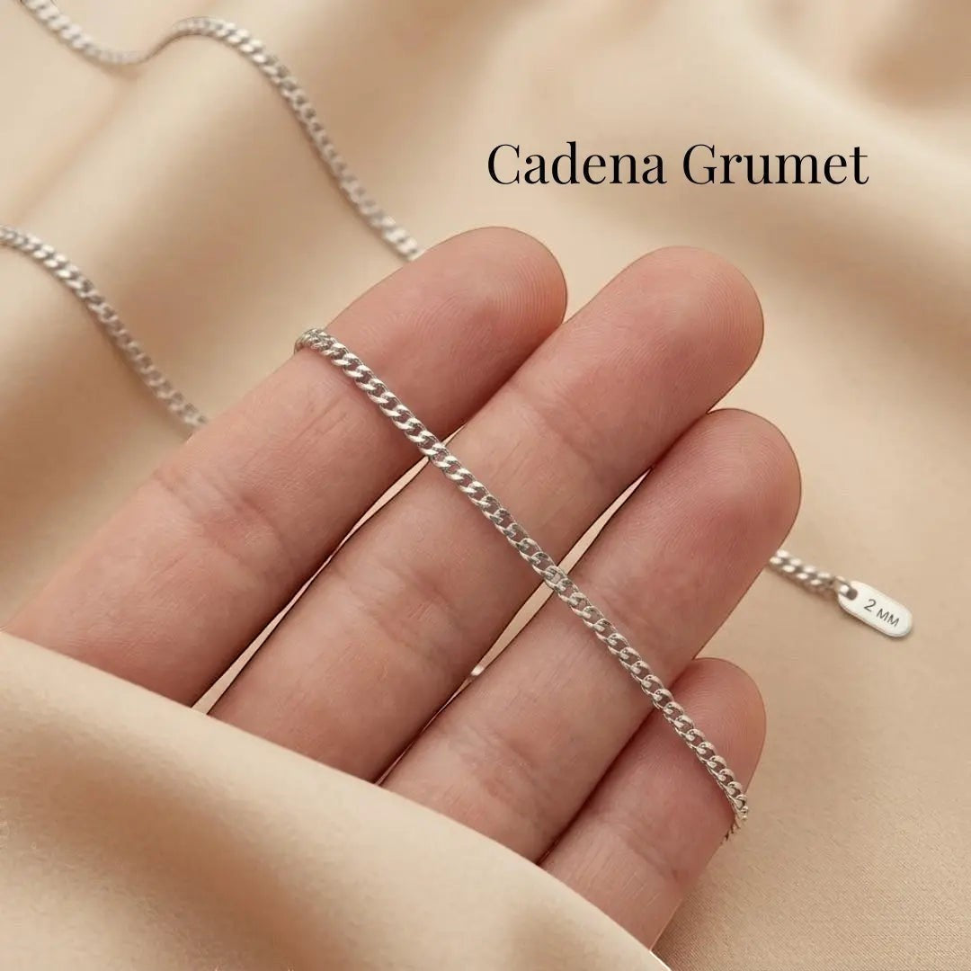 Cadena grumet plateada de acero quirúrgico de Moment sostenida en la mano sobre fondo de tela beige suave