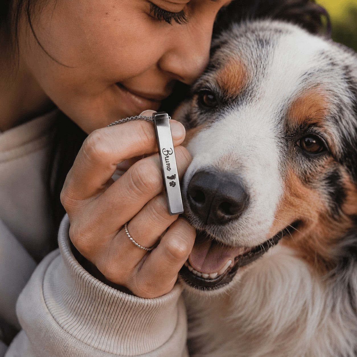 Collar con barra de acero Moment personalizada con nombre y huella junto a una mujer abrazando a su perro