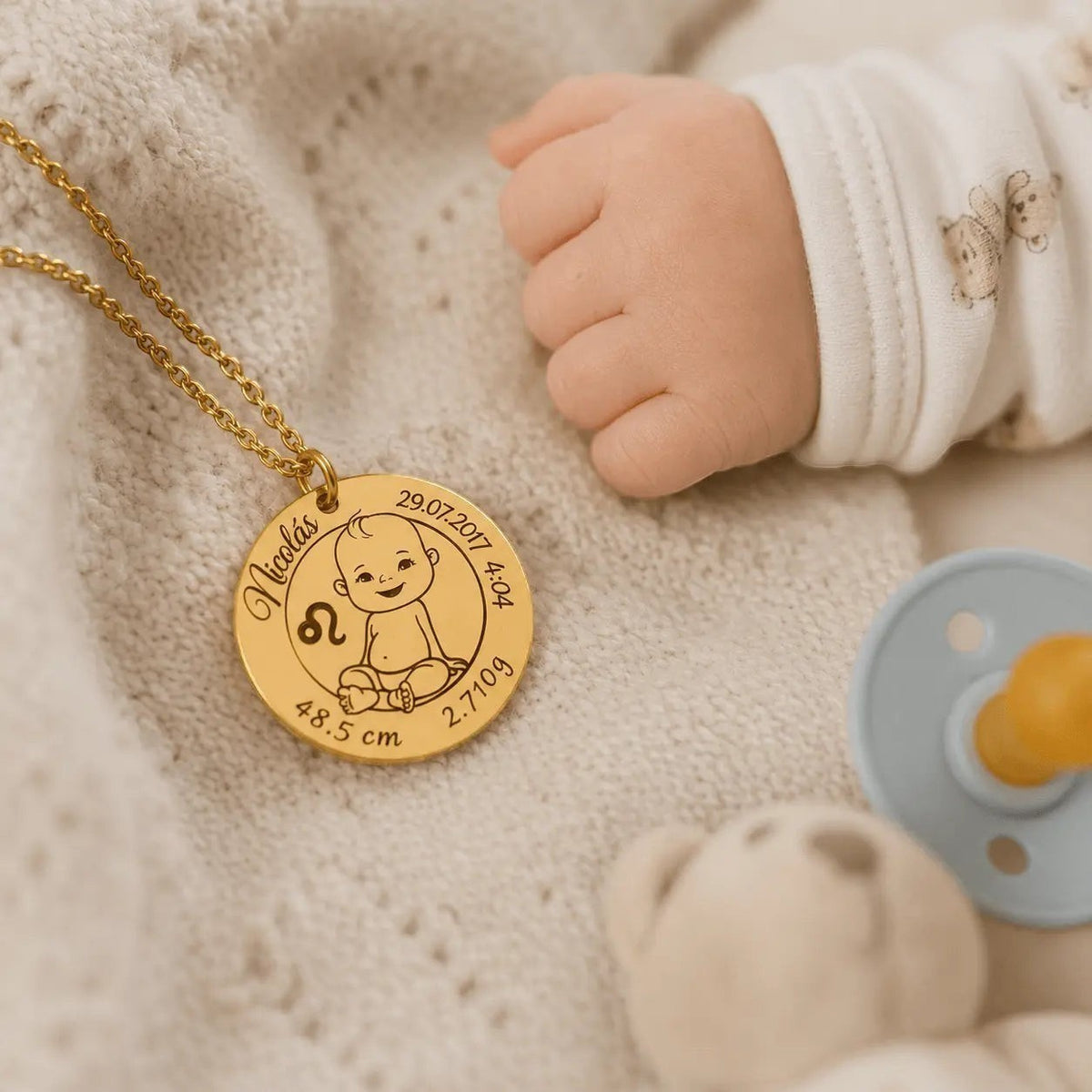Collar Moment dorado de acero inoxidable con medalla grabada con datos de nacimiento de bebé junto a una mano infantil