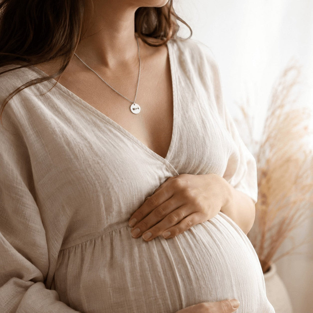 Collar Moment de plata con medalla redonda personalizada sobre mujer embarazada con vestido de lino beige