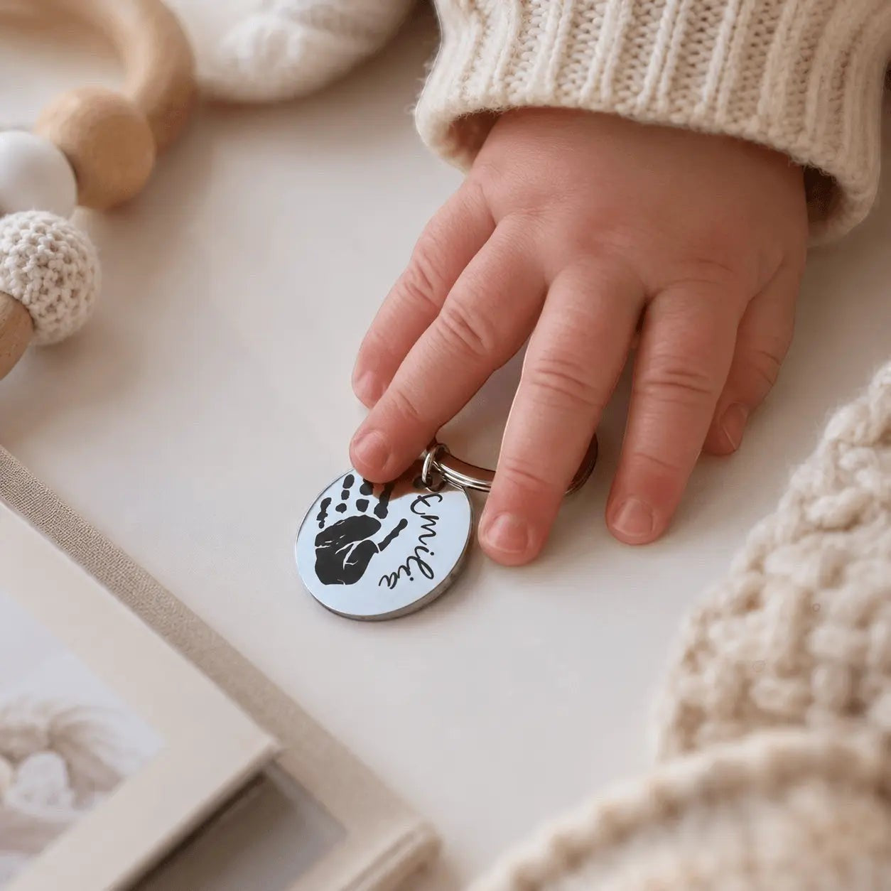 Llavero Moment de acero inoxidable plateado con grabado personalizado de huella y nombre sostenido por mano de bebé