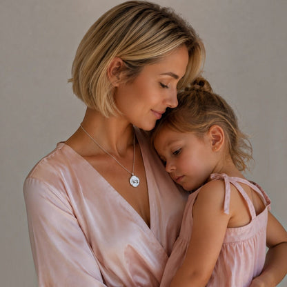 Mujer con su hija luciendo un medallón perfumado Moment de acero inoxidable con grabado de manitos y cadena de 50 cm