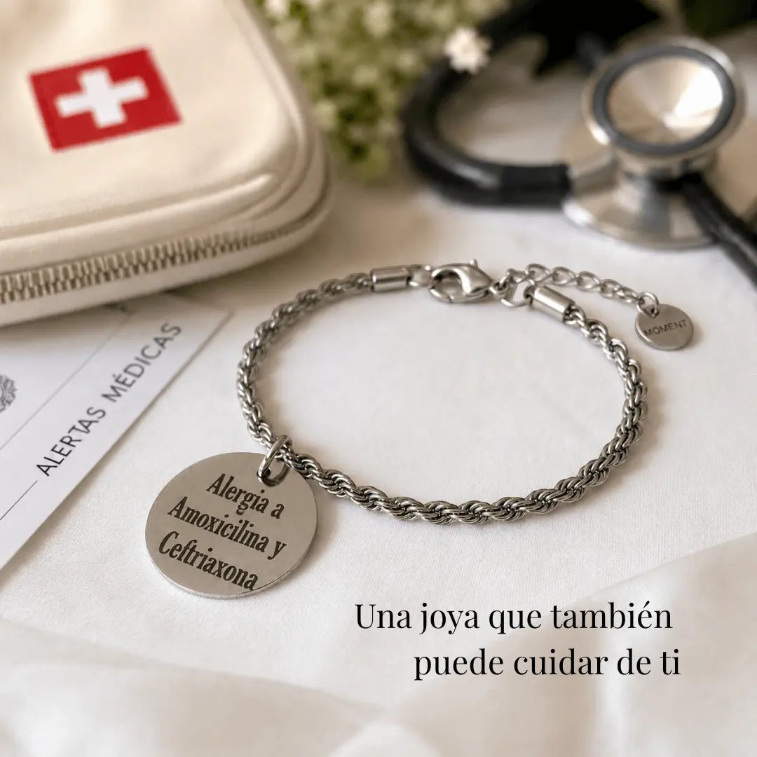 Pulsera Moment de acero inoxidable con medalla grabada de alerta médica sobre fondo blanco con estetoscopio.