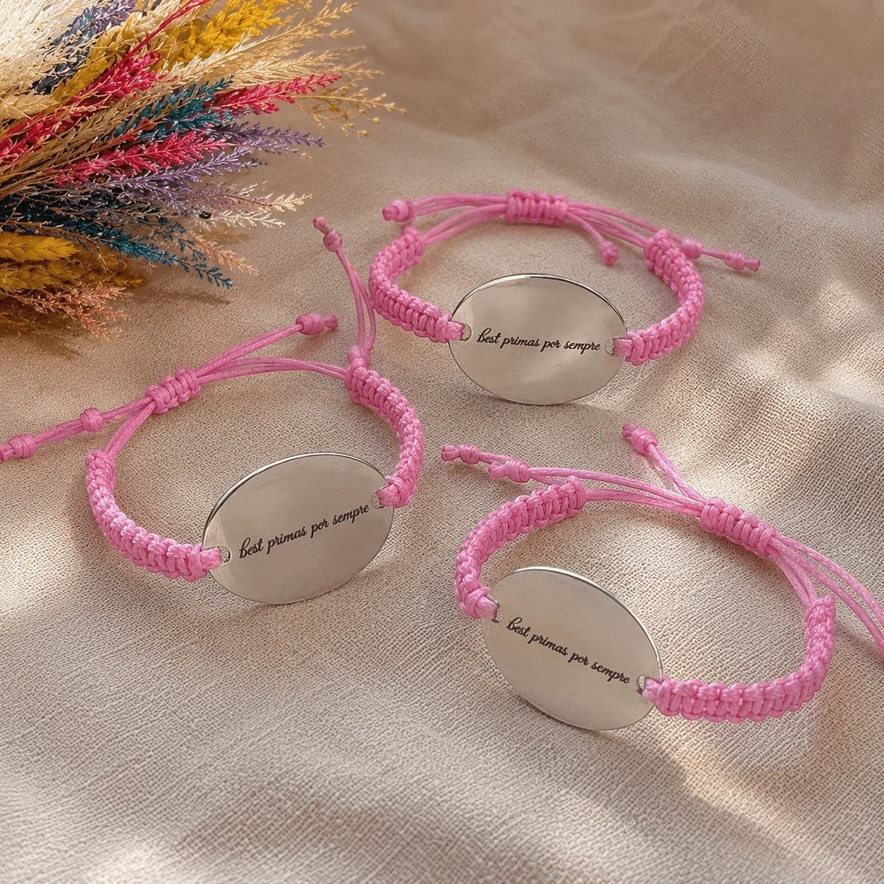 Tres pulseras Moment con placa ovalada de acero inoxidable y cordón rosa ajustable, grabadas con frase personalizada.